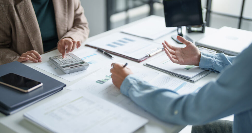 Two people discussing financial documents at a desk with a calculator and laptop.